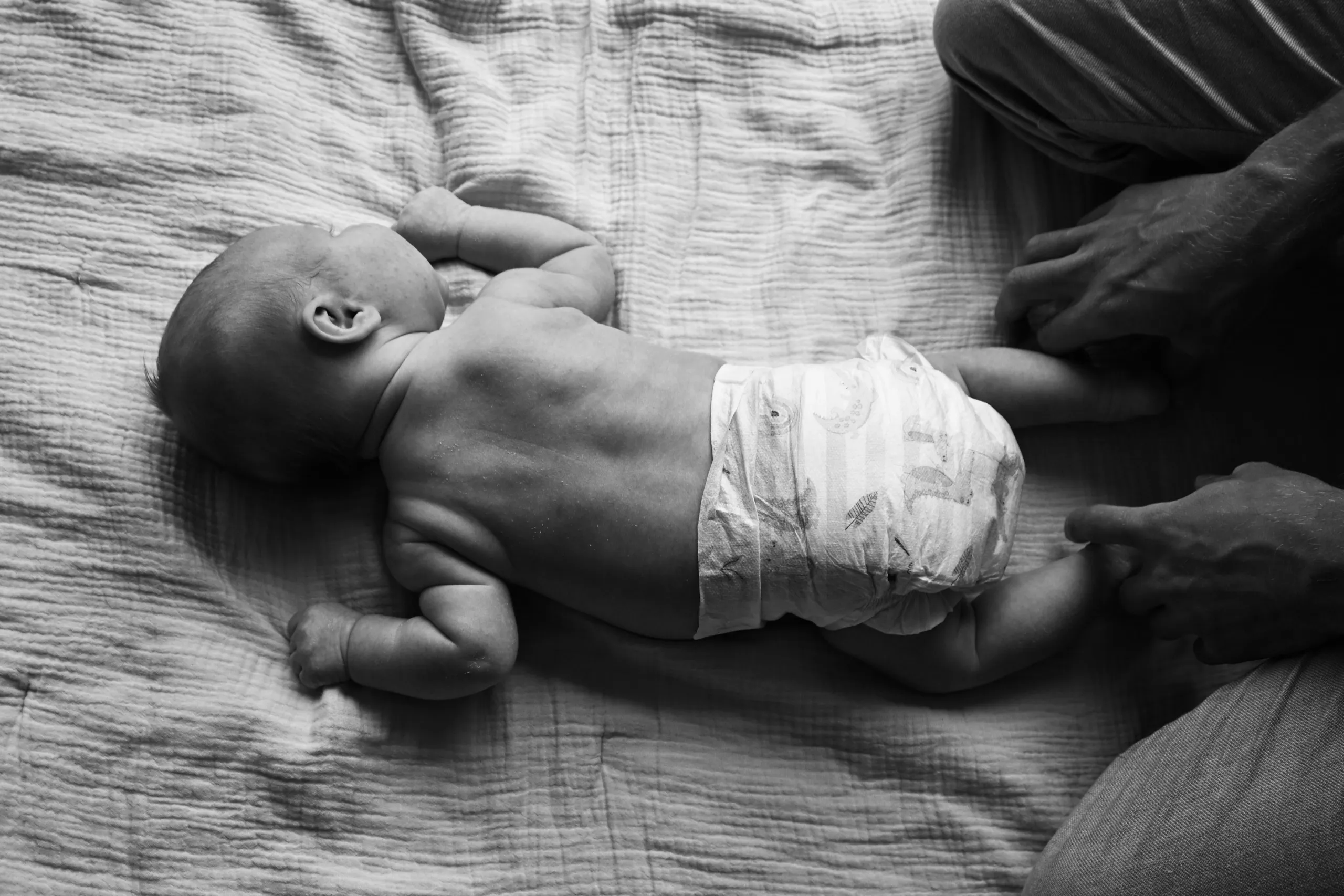 Un nouveau-né allongé sur le lit, une main d’adulte près de lui