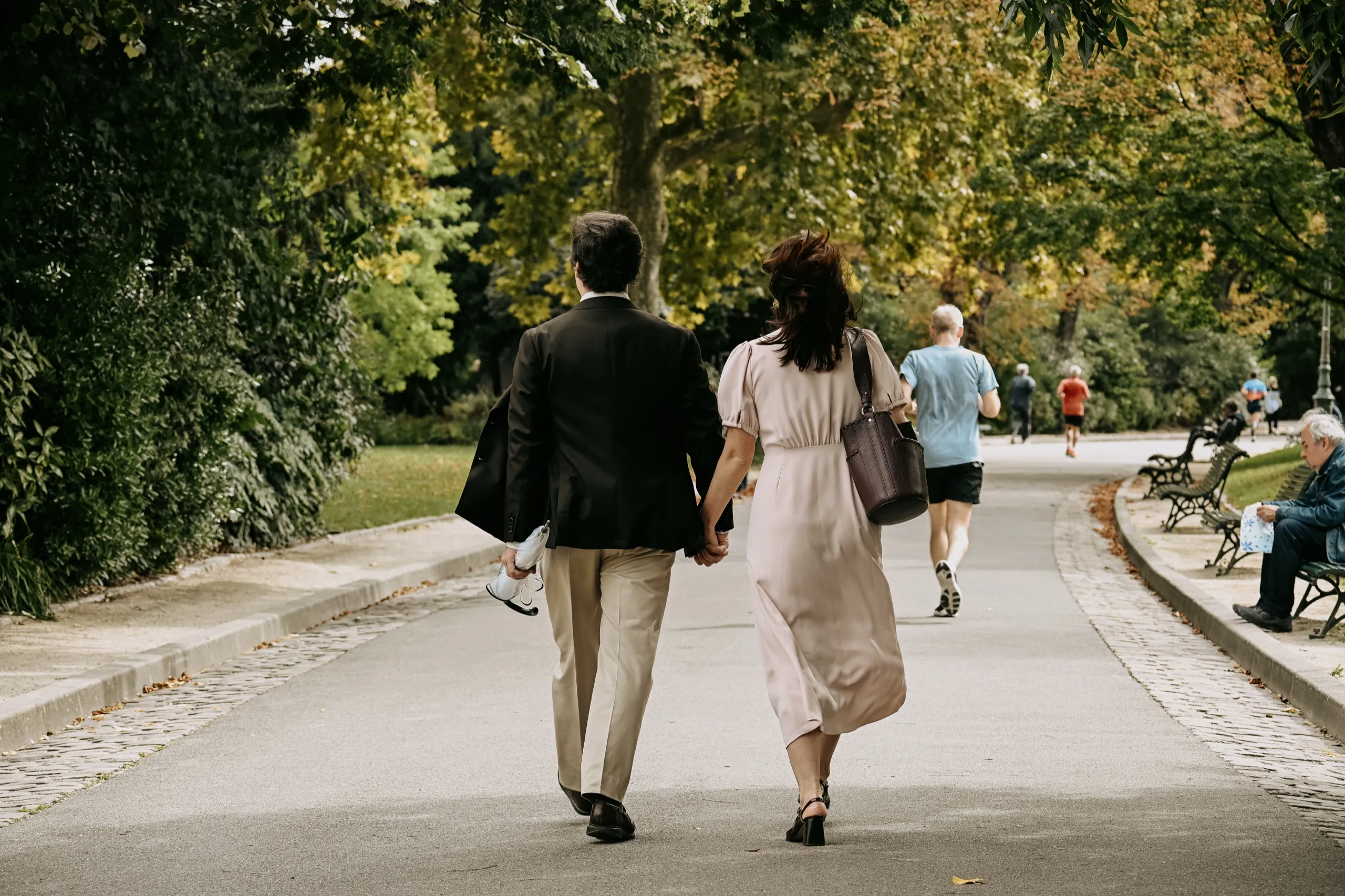 Un couple s’éloigne main dans la main sur une allée bordée d’arbres