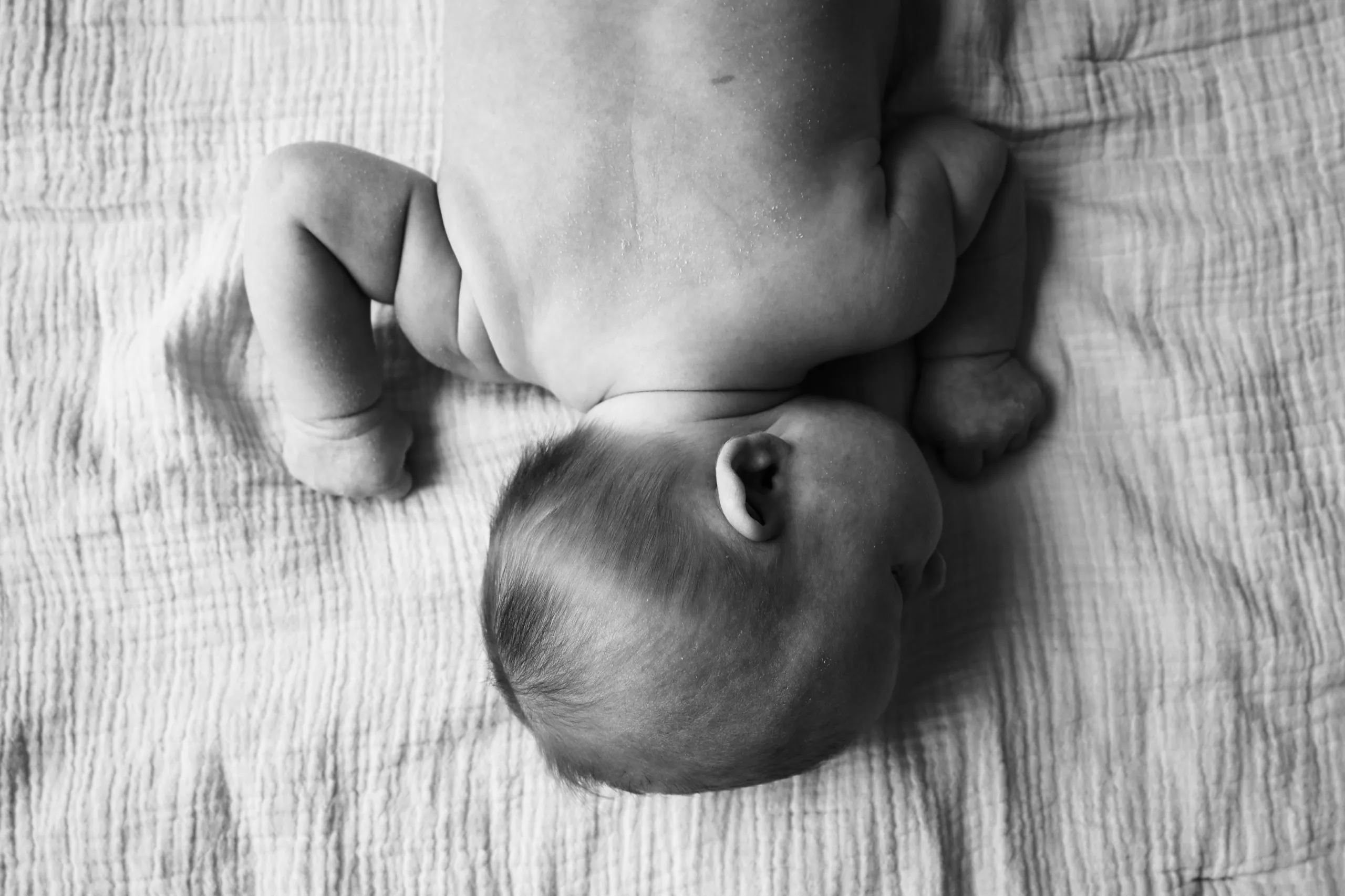 Un nouveau-né allongé, photographié en noir et blanc à la lumière du jour