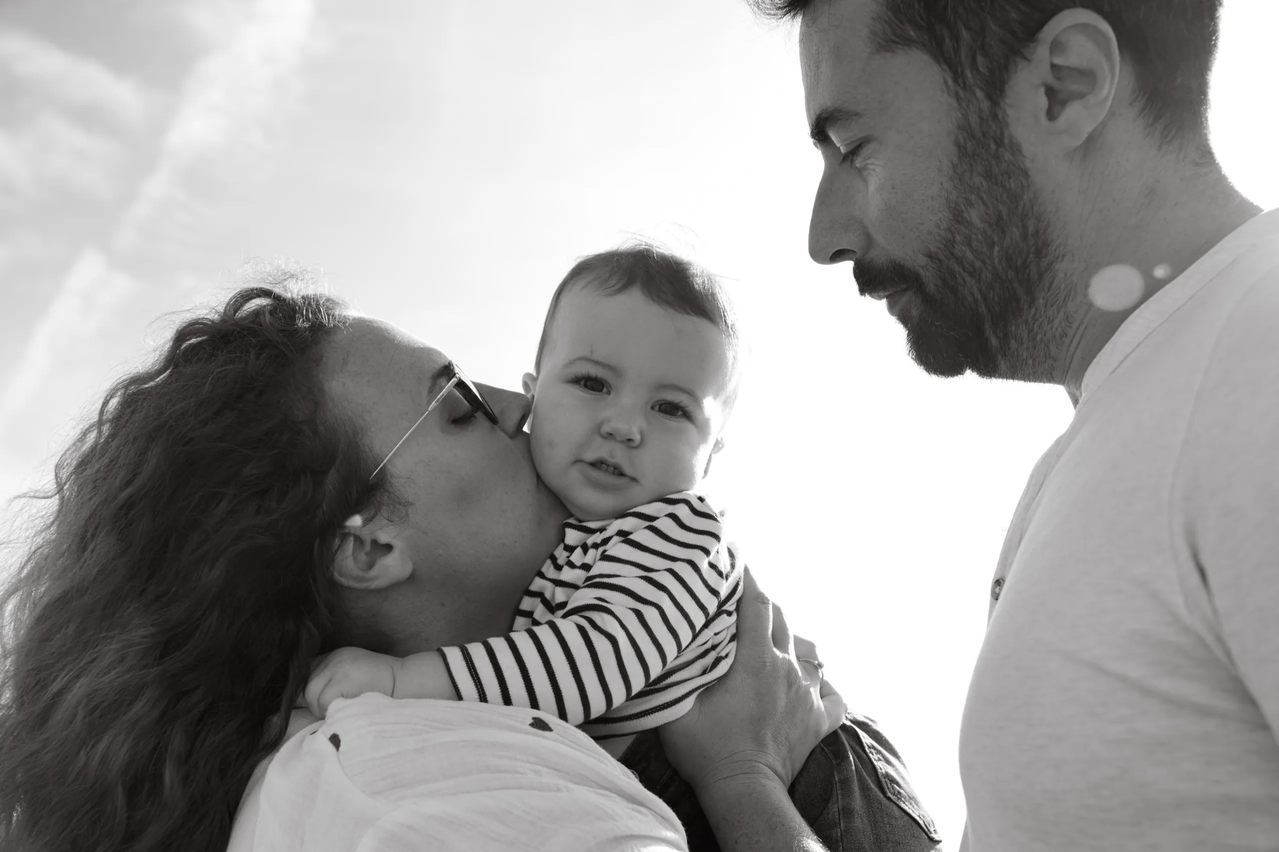 Un bébé dans les bras de ses parents, sa mère l’embrasse sur la joue