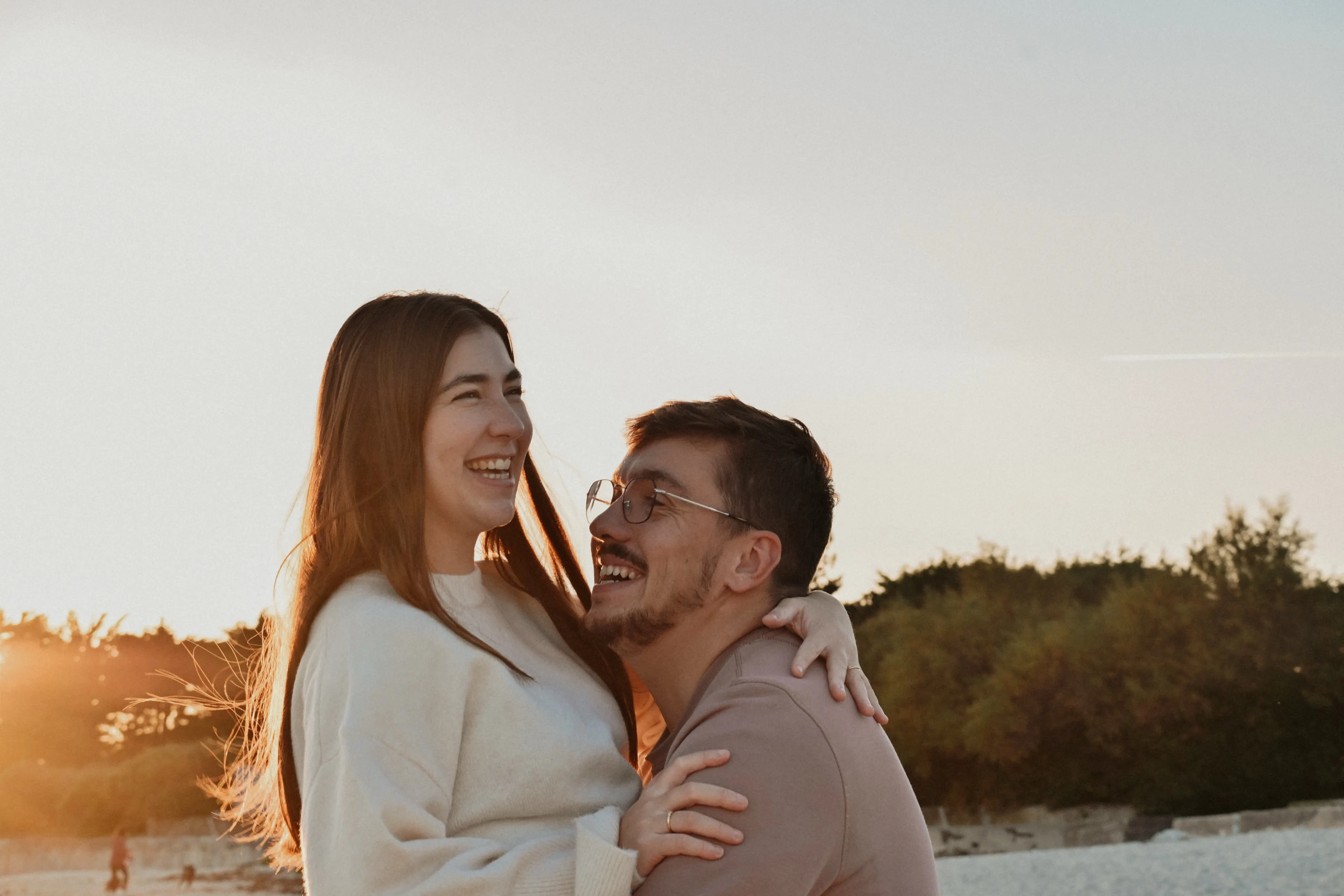 Un couple enlacé qui rit dans la lumière dorée du soir, sur une plage de Bretagne Sud